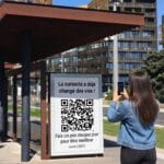 Femme scannant avec son smartphone une affiche d'abribus C3DF, avec le message "La curiosité a déjà changé des vies, fais un pas chaque jour"